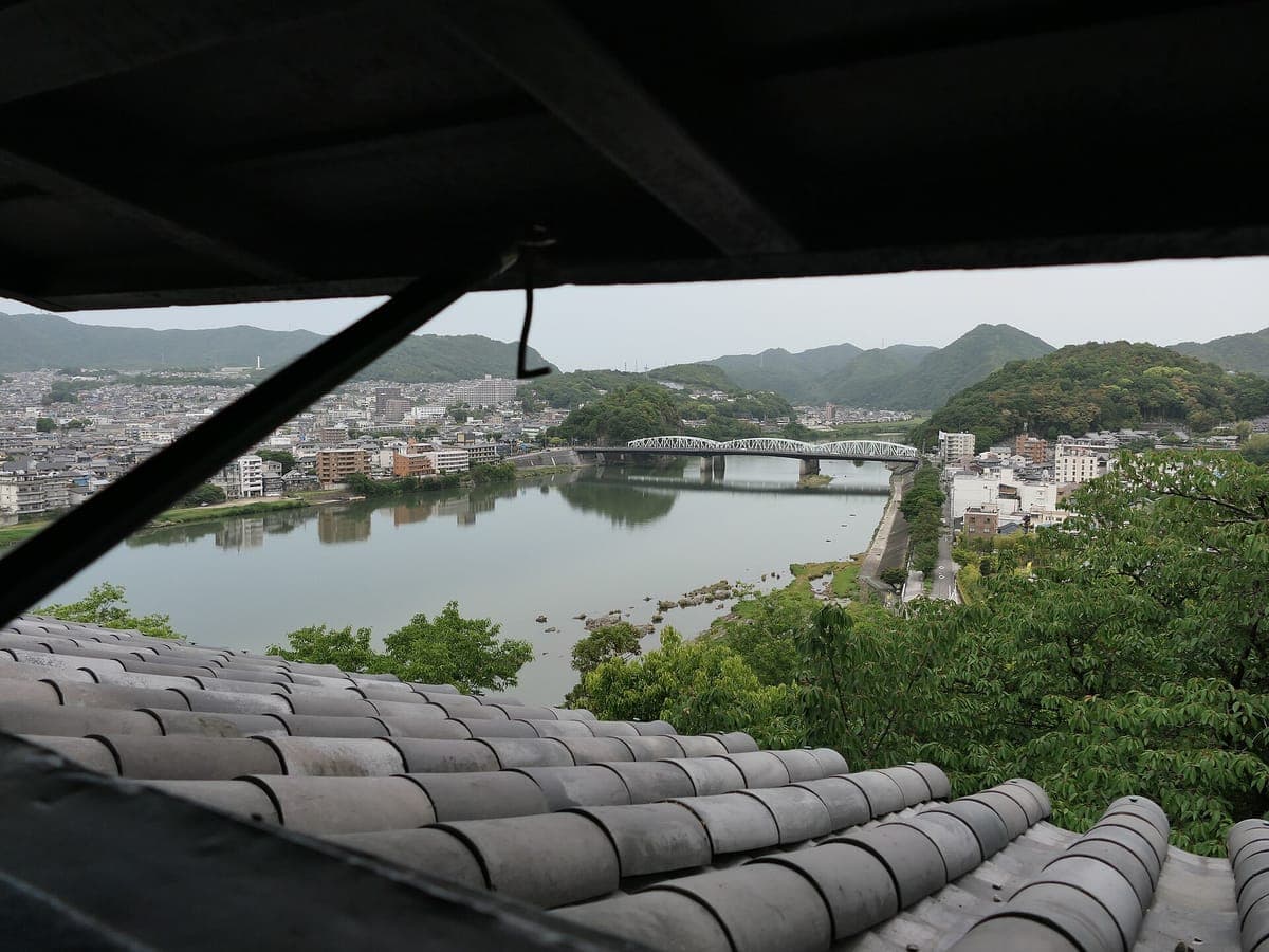 Vista dall'interno del castello di Inuyama sopra le tegole grigie fino al fiume Kiso, un ponte in acciaio bianco e verdi colline sullo sfondo