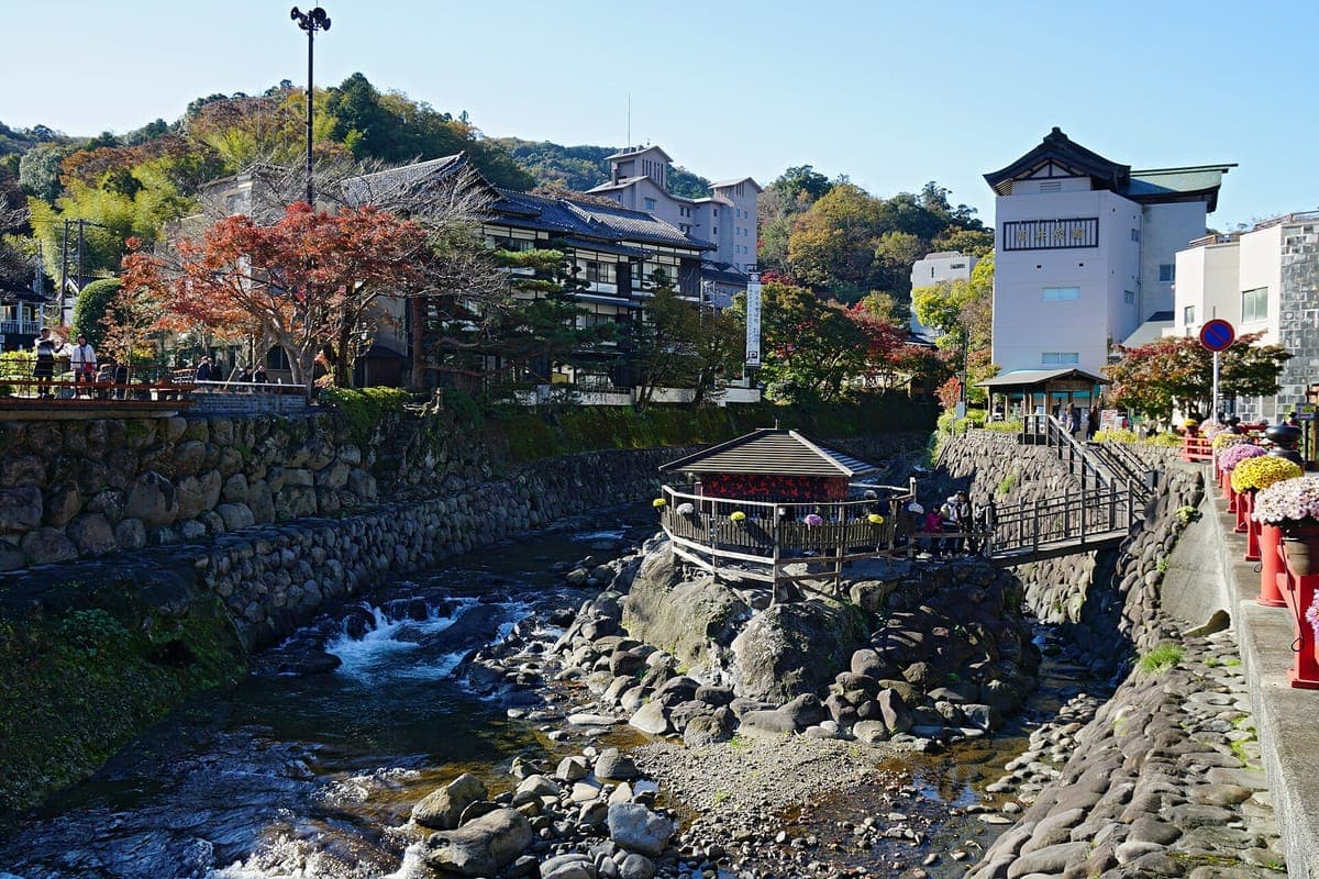 Ang Katsura River na dumadaloy sa ibabaw ng mga bato sa Shuzenji Onsen, na may maliit na bubong na pavilion sa mga bato, mga puno ng taglagas at mga gusali ng ryokan sa tabi ng mga pampang