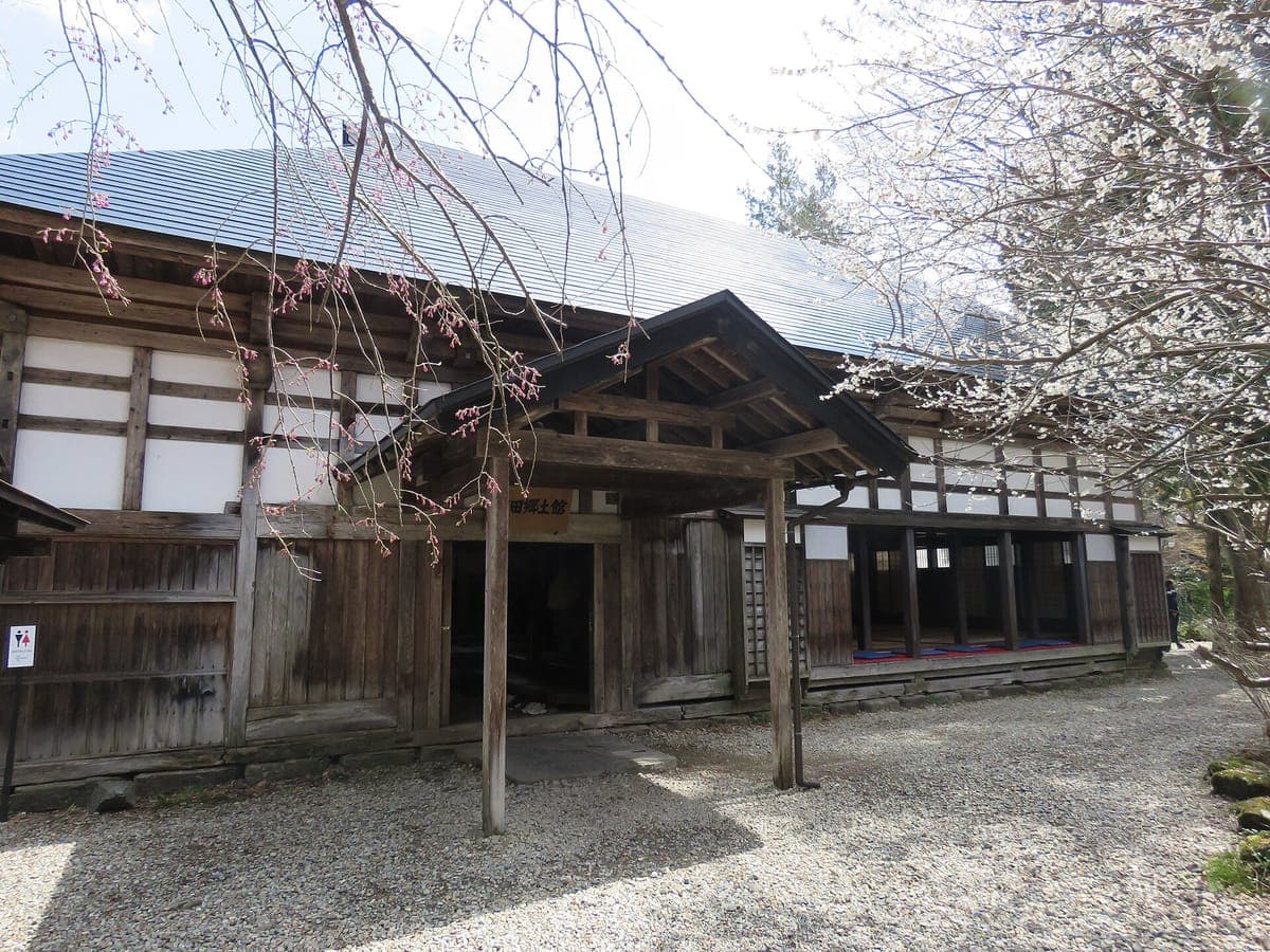 Isang tradisyunal na kahoy na samurai house na may puting plaster panel at malawak na bubong, na nasa harapan ng isang bakuran ng graba, sa Aoyagi house sa Kakunodate