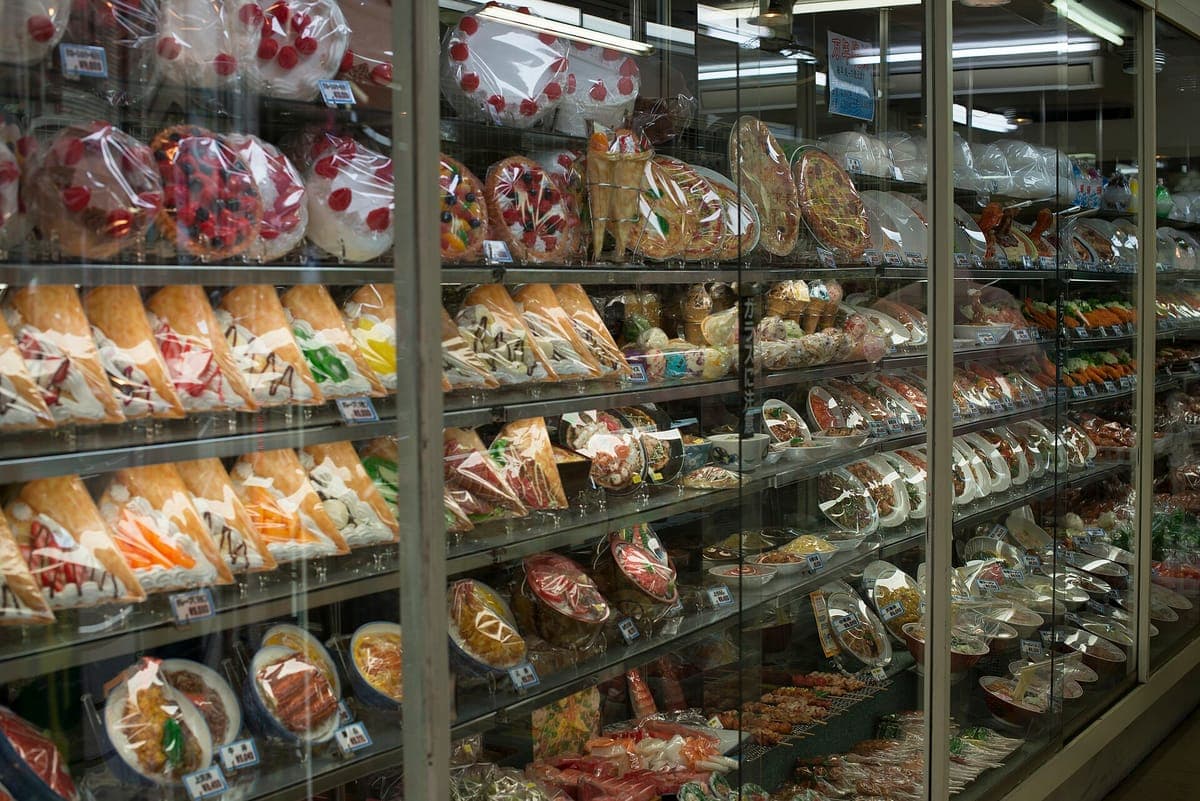 Isang glass display case na puno ng mga hilera ng makatotohanang plastic na sample ng pagkain, kabilang ang mga cake, sandwich, fruit dessert at plated dish