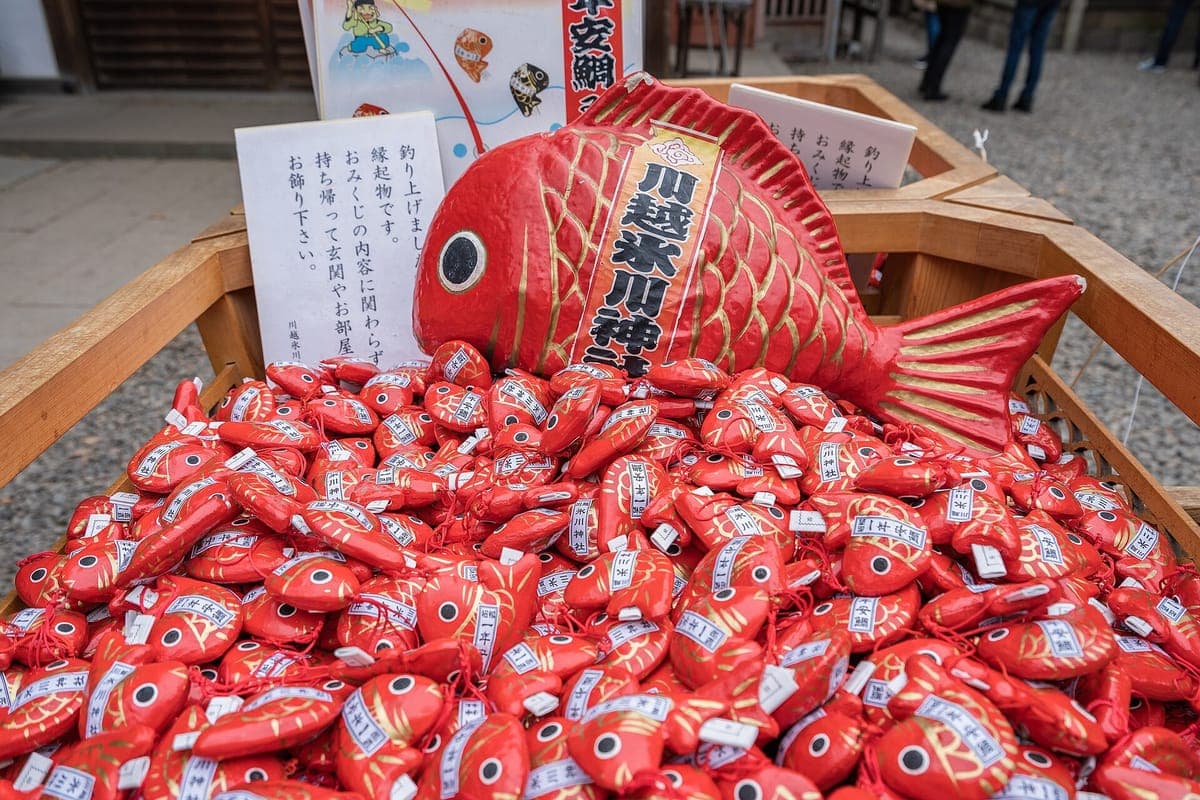 Isang basket na puno ng maliit na pulang papel na sea bream na kapalaran sa Kawagoe Hikawa Shrine, na may malaking modelo ng pulang sea bream sa itaas
