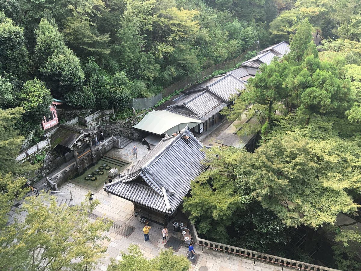 Kiyomizu-dera'daki Otowa şelalesinin yukarıdan görünümü, üç ince derenin döküldüğü, yeşil ağaçlarla çevrili, aşağıdaki yolda ziyaretçilerin bulunduğu çatılı bir köşk.