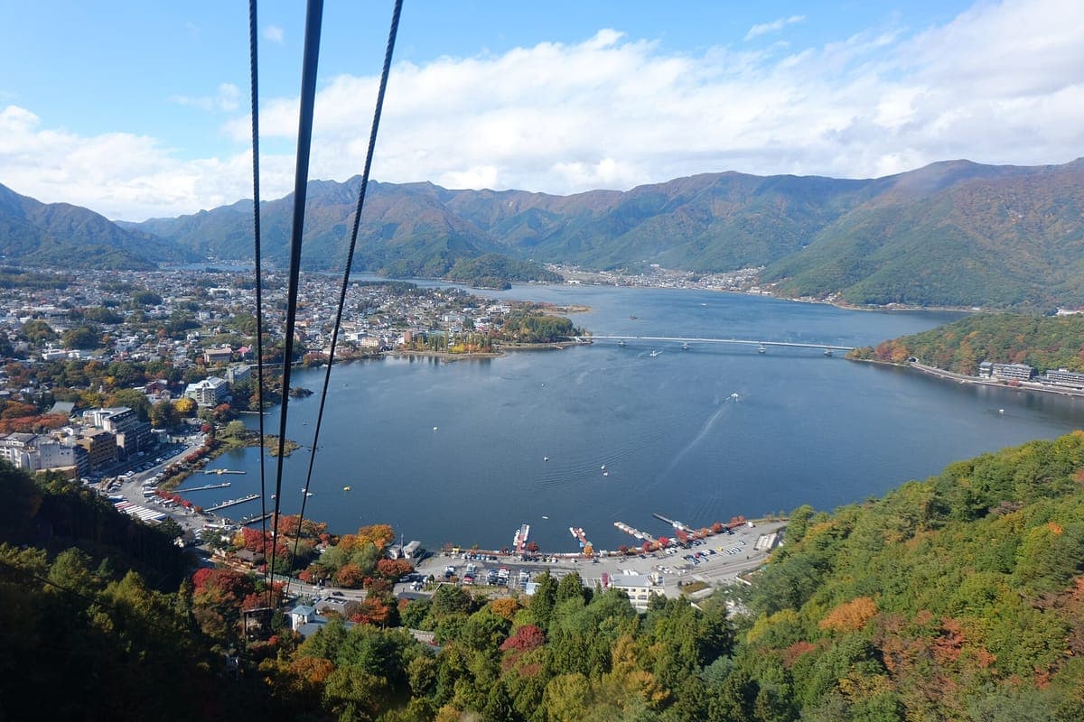 Widok z panoramicznej kolejki linowej na górę Fuji, patrząc w dół na kable nad miastem i błękitną krzywizną jeziora Kawaguchi, z zielonymi wzgórzami i jesiennymi drzewami