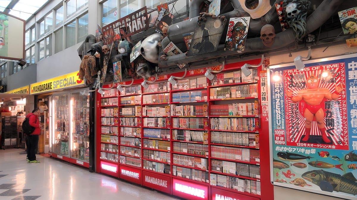 Chodba uvnitř Nakano Broadway lemovaná červeně orámovaným Mandarake obchodem plným manga regálů s postavami a plakáty, které se tísní nad stěnou