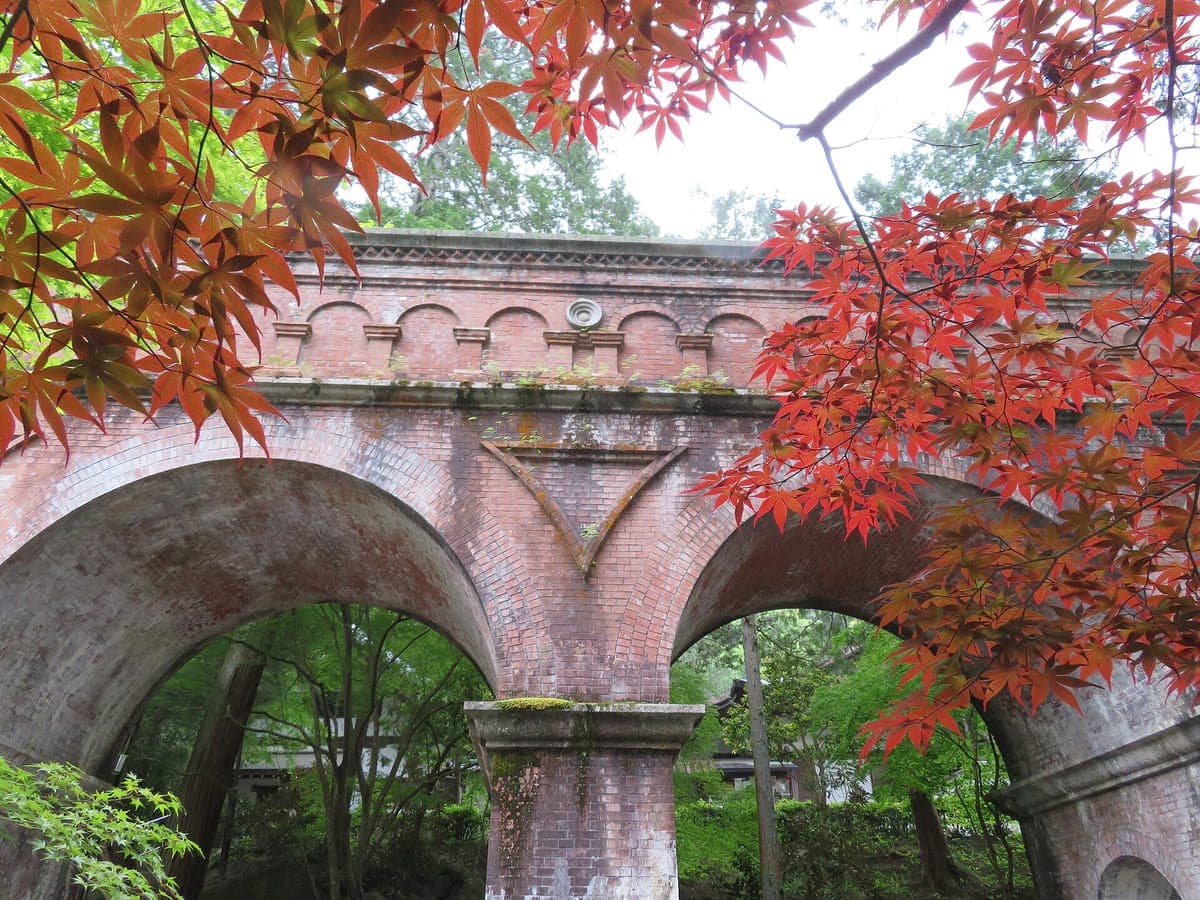 Arches d'un aqueduc en briques rouges patinées à Nanzen-ji, encadrées par des feuilles d'érable rouge vif