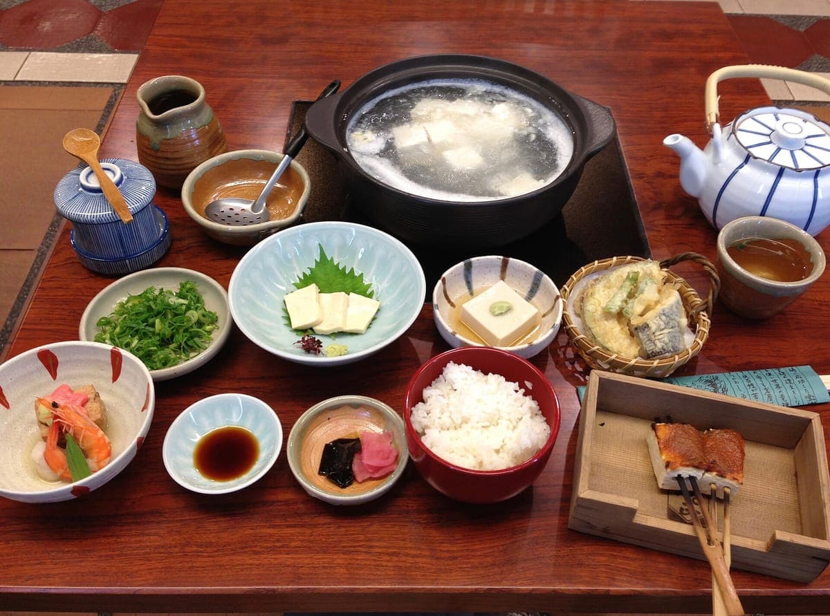 Un yudōfu repas préparé sur une table laquée : une marmite de tofu dans un bouillon clair sur un brûleur, du riz, du tempura, des légumes saumurés et plusieurs petits accompagnements