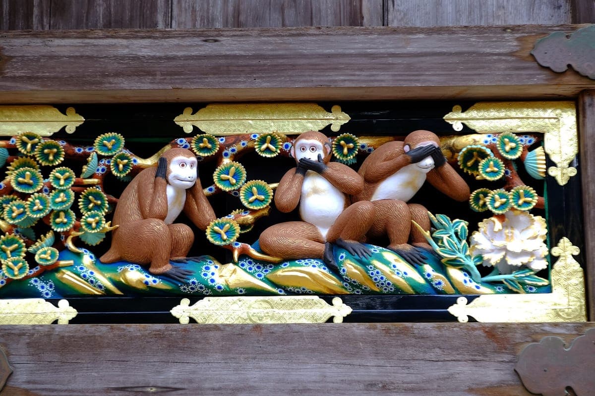Vyřezávaný a malovaný panel tří moudrých opic v Nikkō Tōshōgū, z nichž jedna si zakrývá oči, druhá ústa a druhá uši, mezi zelenými listy