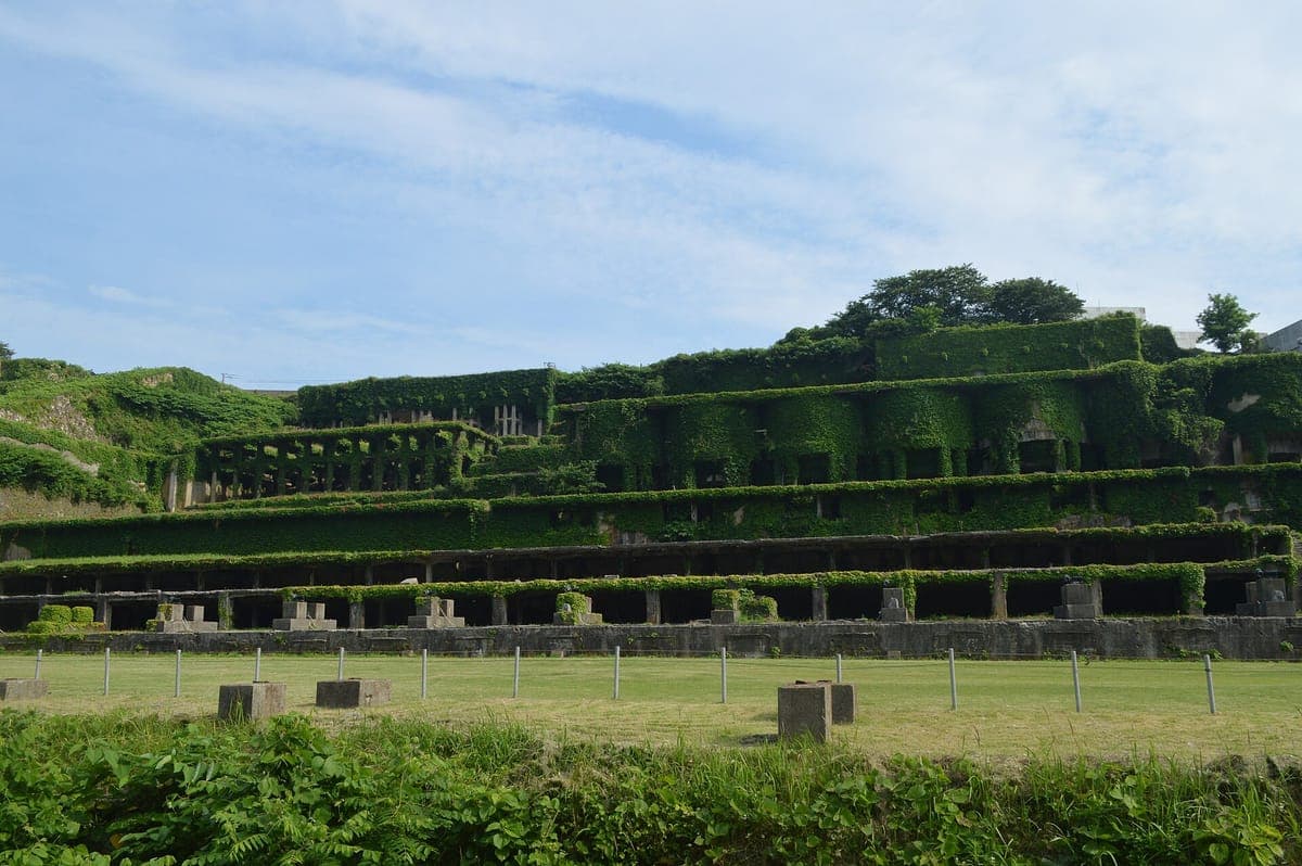 De betonnen terrassen van de Kitazawa Flotation Plant-ruïnes op het eiland Sado, bedekt met groene vegetatie, met een gazon ervoor en een blauwe lucht erboven
