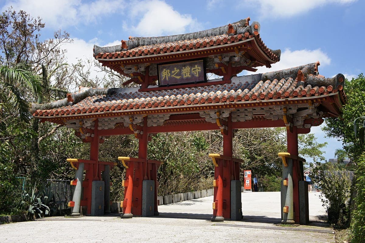 La puerta Shureimon del castillo Shuri con pilares rojos, dos hileras de techos de tejas naranjas y una tablilla con caracteres chinos