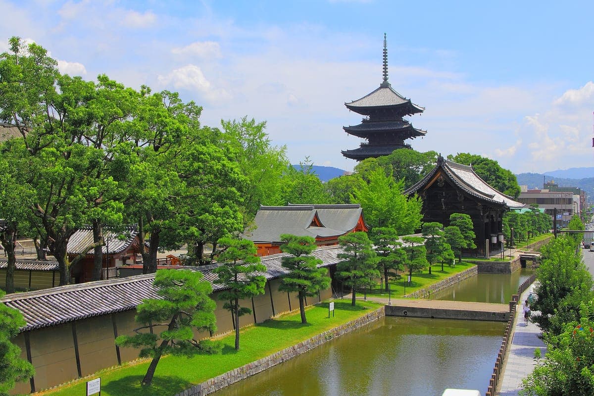 La oscura pagoda de madera de cinco pisos de Tō-ji se eleva sobre los pinos y los tejados de los templos, con un foso de agua verde en primer plano.
