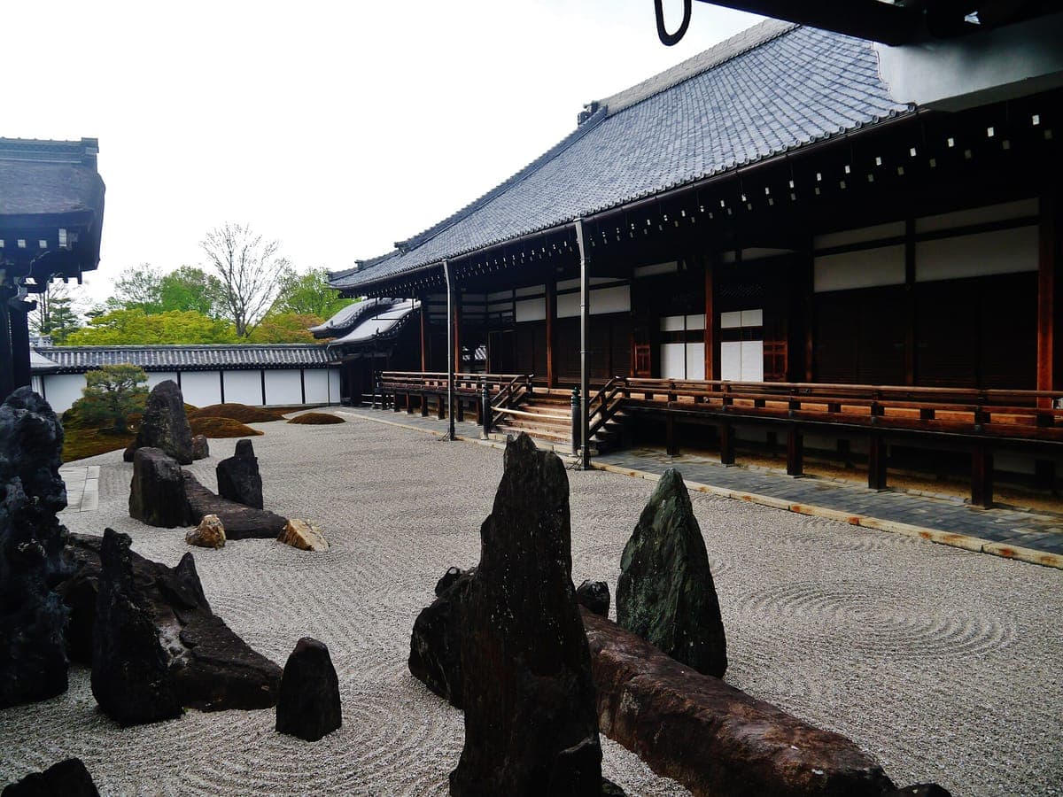 Mga patayong maitim na bato na umaangat mula sa naka-raket na puting graba sa harap ng mahabang kahoy na veranda ng kwarto ng abbot sa Tōfuku-ji