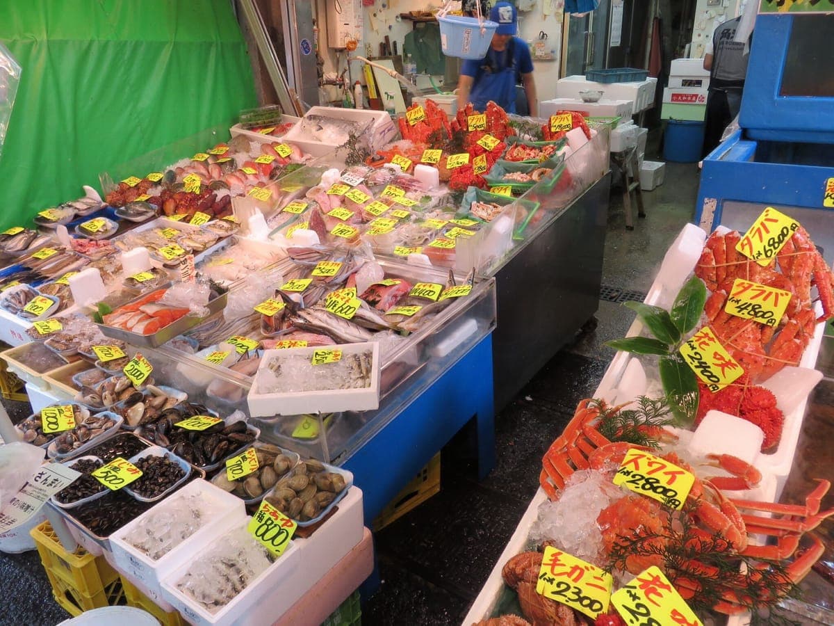 Isang seafood stall sa Tsukiji Outer Market na may mga tray ng shellfish, crab at isda sa yelo sa ilalim ng dilaw na label ng presyo