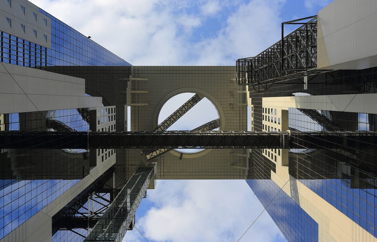 Mirando hacia arriba entre las dos torres del Umeda Sky Building, el observatorio en forma de anillo y los tubos de las escaleras mecánicas que cierran la brecha contra un cielo azul.